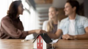Couple shaking hands with broker, toy house in foreground