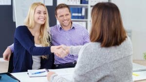 Happy couple shaking hands with a female business broker or investment adviser as they attend a meeting in her office