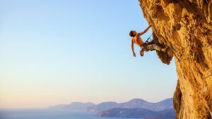 Photo of man climbing a cliff face with peninsula in the background