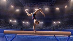 Female athlete doing a complicated exciting trick on gymnastics balance beam in a professional gym. Girl perform stunt in bright sports clothes
