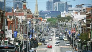 Dec 25th 2017, suburban area of Melbourne with shops have Victorian facades along the street and city high-rise skyscrapers view in distance. Cars share traffic with trams. Brunswick, VIC Australia.