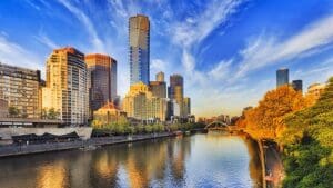 Tallest Melbourne skyscraper Eureka tower dominates South Yarra cityscape over Yarra river in warm morning sunlight under blue sky.