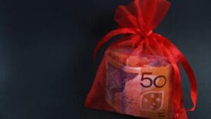 A red bag holding a wad of cash or currency. 50 fifty dollar note clearly visible through bag. Gift, financial assistance, support and bonus concept. Lottery winnings, fairytale result from business
