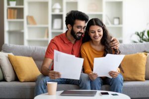 Happy young Indian couple checking documents at home on the couch